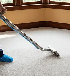 Steam carpet cleaning technician using a hot-water extraction wand on a residential carpet, wearing blue protective shoe covers Columbia, SC.