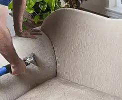 Professional upholstery cleaner deep-cleaning a fabric sofa with a handheld extraction tool and hose in Columbia, SC.